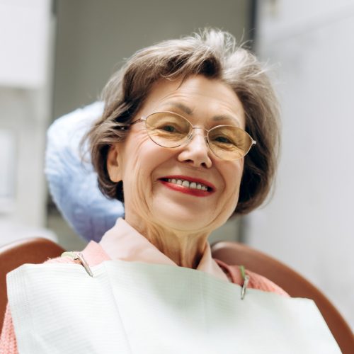 naccid-buford-dentist-dental-concerns-with-porcelain-fixed-bridges A senior woman smiles at the camera in her dentist's office- naccid, buford dentist, ga