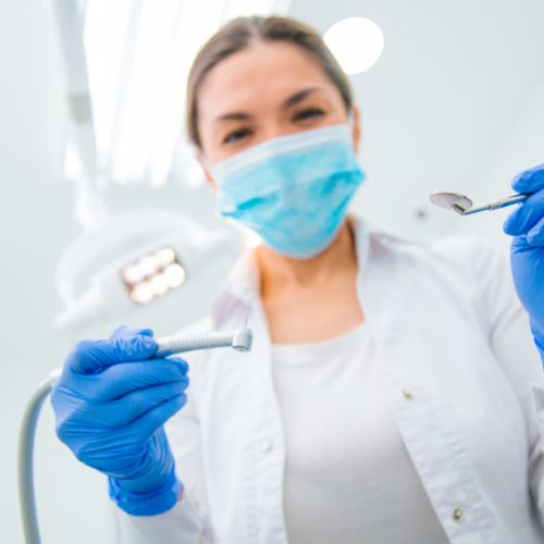 A female dentist wears a mask as she holds dental cleaning instruments- naccid buford dentist